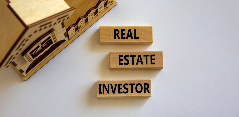 Three wooden blocks with the worlds "Rea; Estate Investor" in front of a wooden house