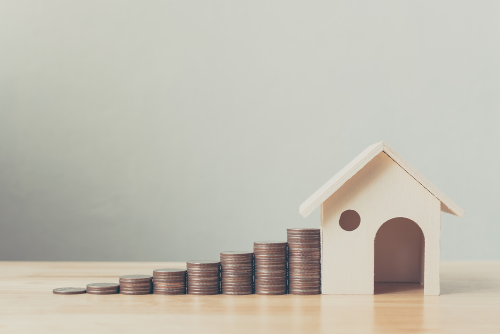 Property investing concept: Increasingly high stacks of coins next to a wooden model house