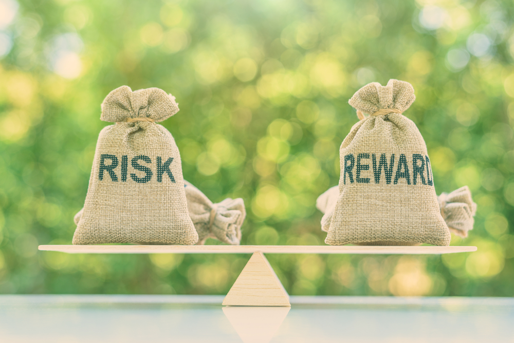 Two burlap sacks labelled "Risk" and "Reward" on either side of a perfectly balanced wooden scale