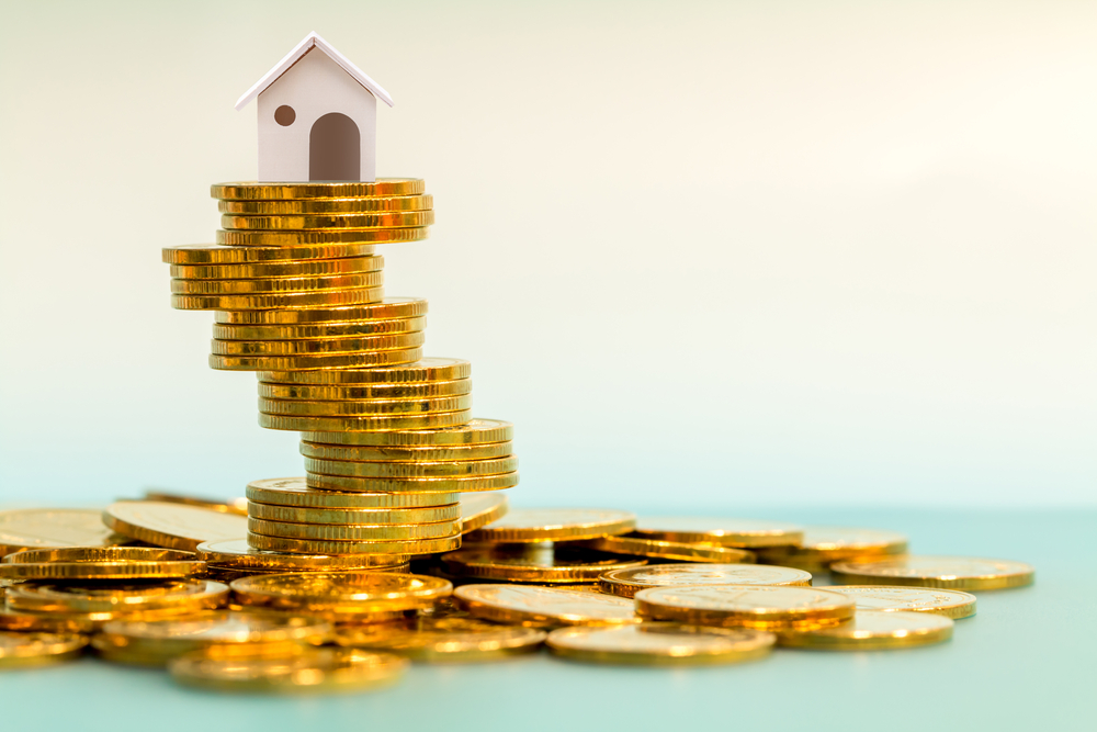 Model house on top of a large pile of gold coins