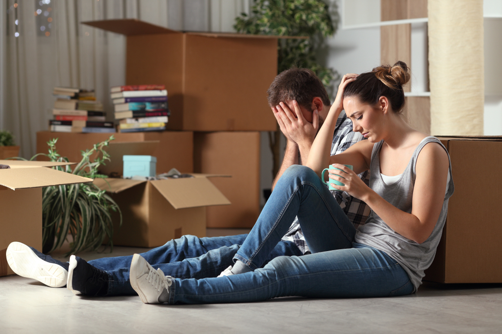 Sad evicted couple sitting on the floor with moving boxes: Disadvantages of investing