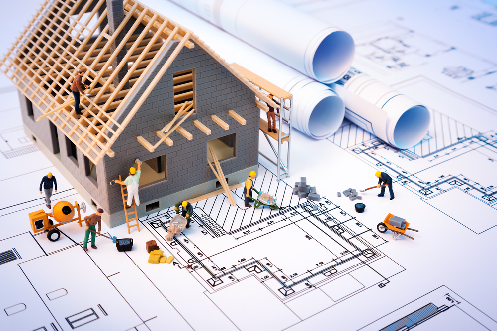 Mini house on blueprints with workers constructing the house